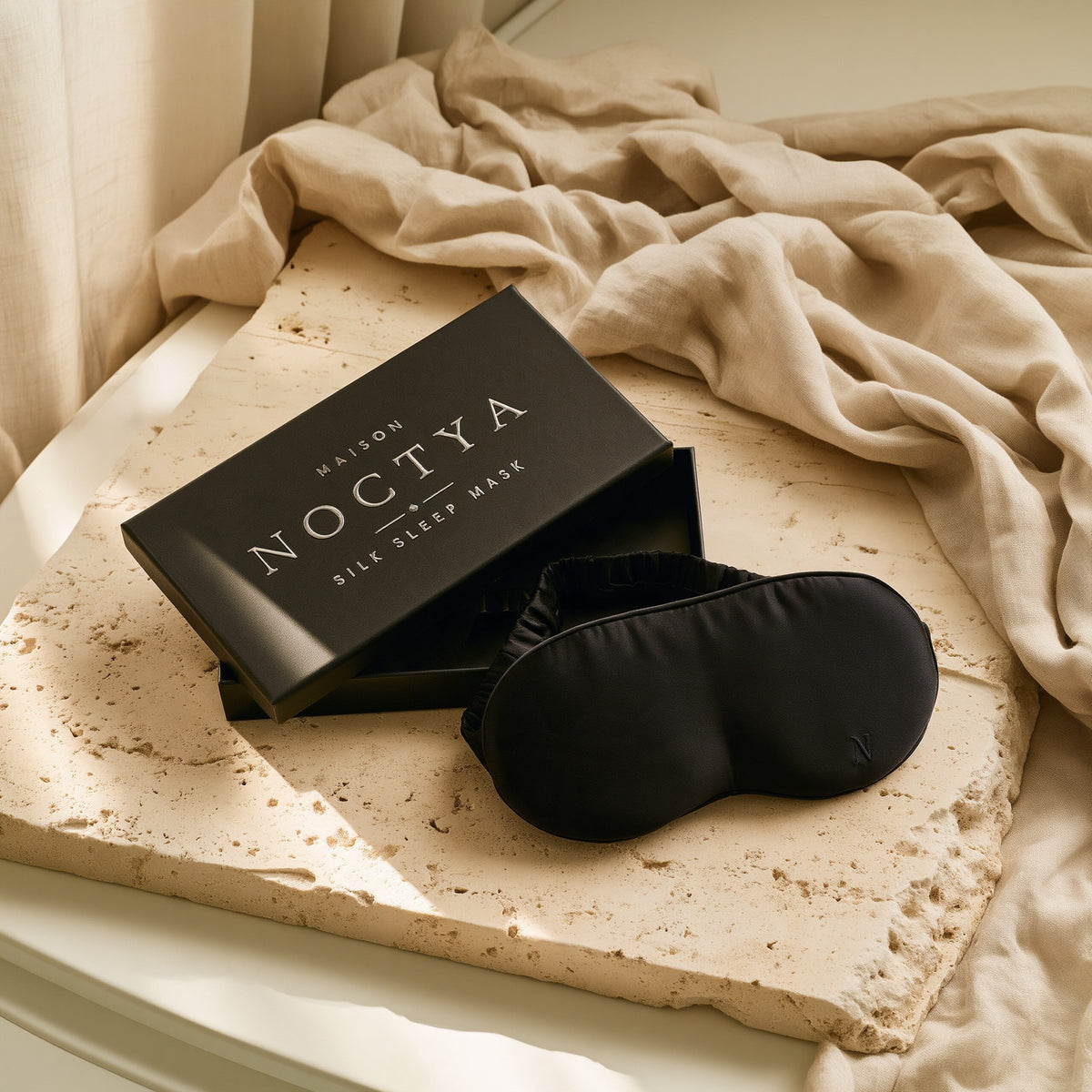Masque de nuit en soie Noctya, coloris Nuit, avec son écrin noir, sur travertin