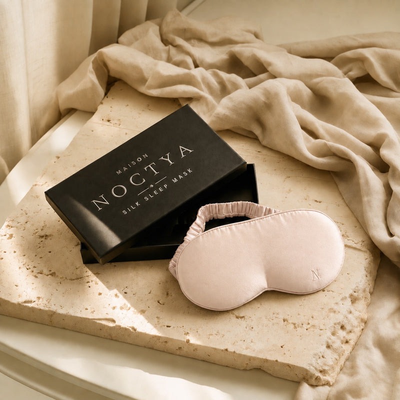Masque de sommeil en soie Noctya, coloris Aube, avec son écrin noir, sur travertin