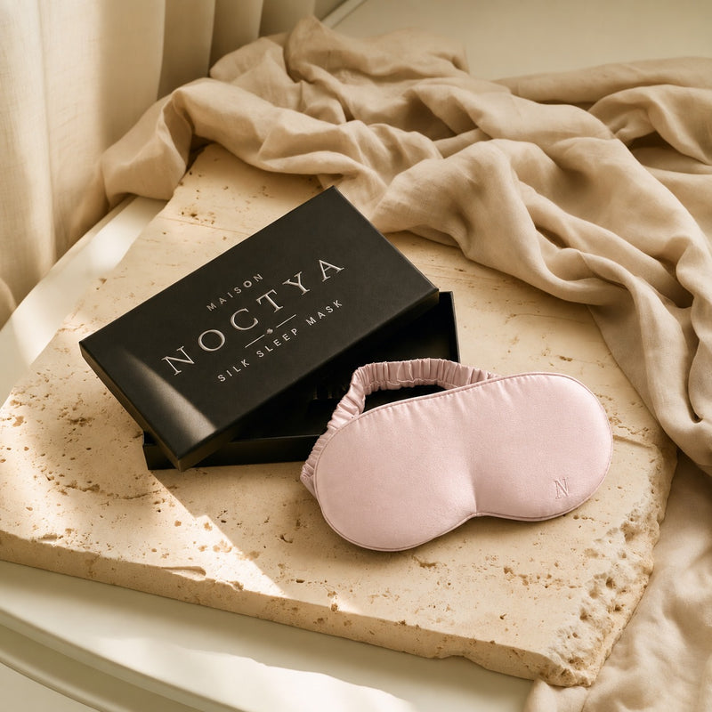 Masque de sommeil en soie Noctya, coloris Poudre, avec son écrin noir, sur travertin